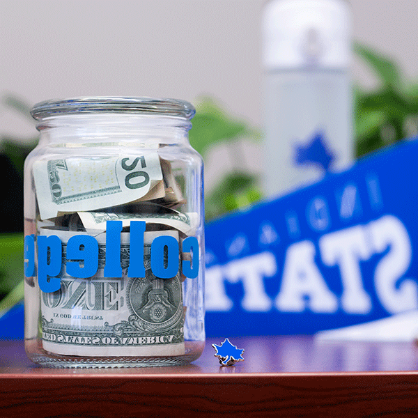 A jar filled with United States currency on a table with a blue Indiana State University penant in the background.  