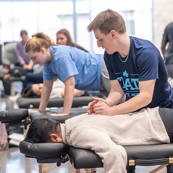 A massage therapy male student performs a massage in the hallway of the Health and Human Services building as part of a series of free sessions open to faculty, students and staff.