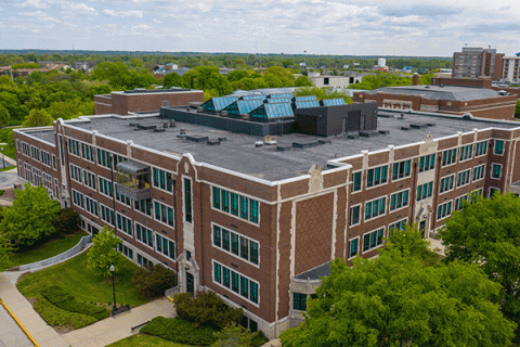 Aerial image of a large, square, brick three-story building in summer